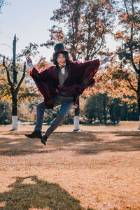 Man cosplaying mad hatter jumping against sunlight and trees