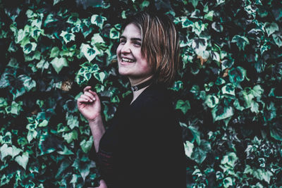 Smiling young woman standing against plants