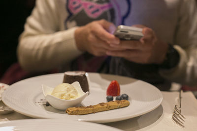 Close-up of dessert in plate against person using mobile phone