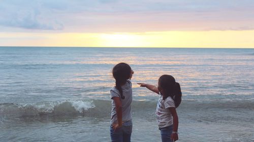 Siblings pointing at sea during sunset