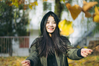 Portrait of smiling young woman standing against tree