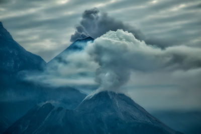 Scenic view of smoke emitting mountains against sky