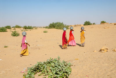 Women carrying pots on head while walking on sand at remote desert