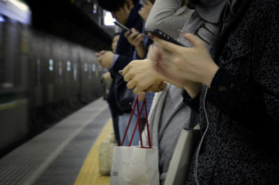 Midsection of people using mobile phone while standing on railroad station platform