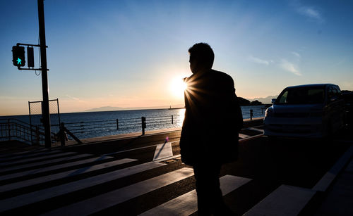 Rear view of silhouette man standing by sea against sky