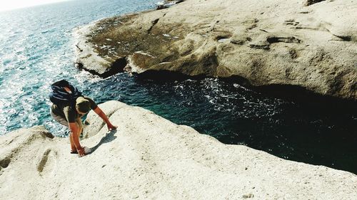 High angle view of mature man with backpack climbing rock by sea