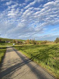 Empty road amidst field against sky