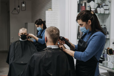 Female barber cutting hair of customer in saloon