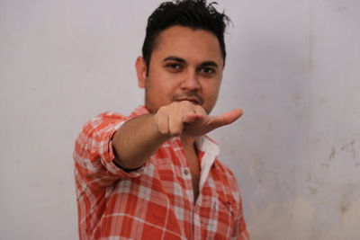 Close up of a young man in orange shirt pointing fingers towards camera