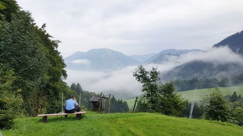 Man sitting on mountain against sky