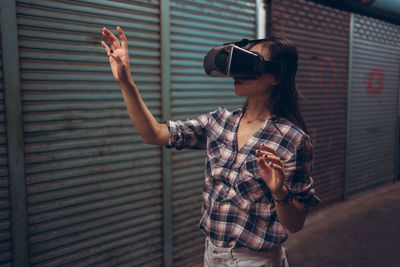 Calm female standing on narrow shabby street and experiencing virtual reality while wearing wireless vr goggles