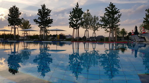 Swimming pool by lake against sky at sunset