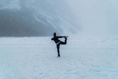 Female ice skater skating on frozen lake outside in snowstorm near forest in canada.