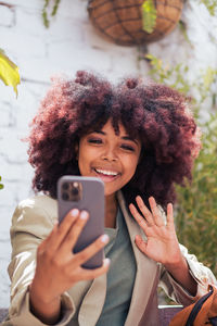 Cheerful african american female manager smiling and waving hand while making video call via cellphone on street