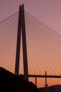 Low angle view of silhouette suspension bridge against clear orange sky
