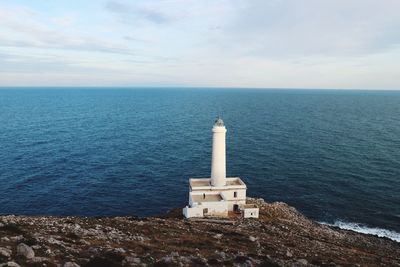 Lighthouse on cliff by sea against sky