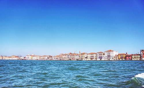 Buildings by sea against clear blue sky