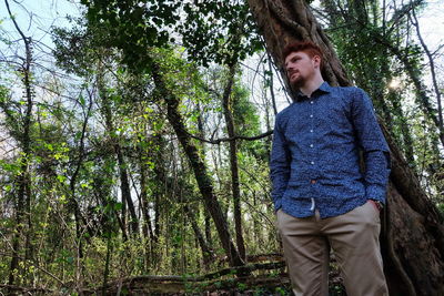 Portrait of young man standing by tree against sky