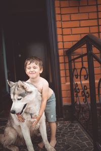 Happy shirtless boy playing with german shepherd on doorway