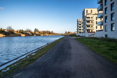 Road by buildings in city against clear blue sky