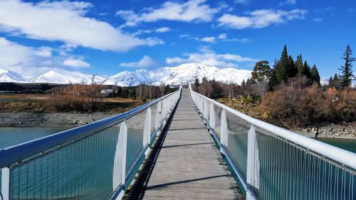 Footbridge leading towards mountains against sky