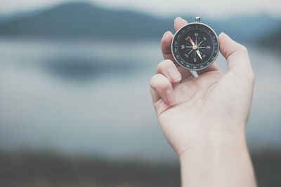 Close-up of hand holding clock against blurred background