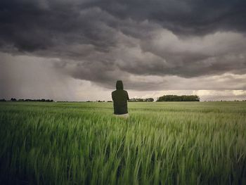 Rear view of man standing on field against cloudy sky