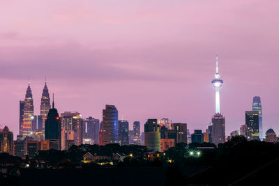 Illuminated buildings in city against sky during sunset