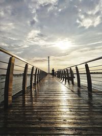 Footbridge over sea against sky during sunset