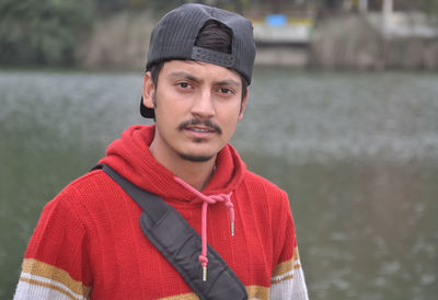 Close-up of a young guy wearing cap backwards looking at camera while standing by the lake