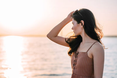 Young woman standing at beach against sky