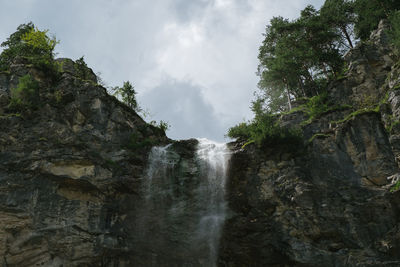 Low angle view of waterfall in forest against sky
