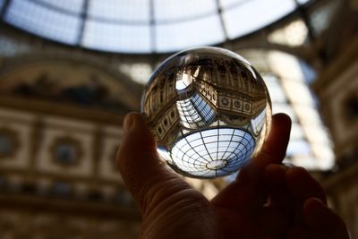 Cropped hand holding crystal ball against glass ceiling 