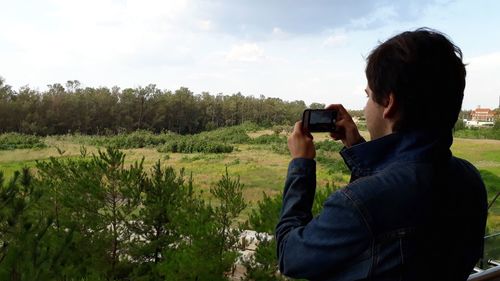 Man photographing with mobile phone against trees