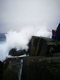 Waves splashing on rocks against sky