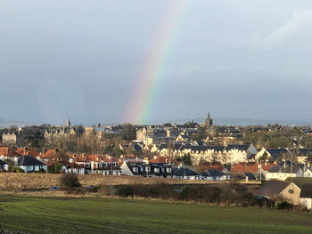 Rainbow over town by buildings in city against sky