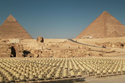 Empty chairs by sphinx and pyramid of khafre against clear sky