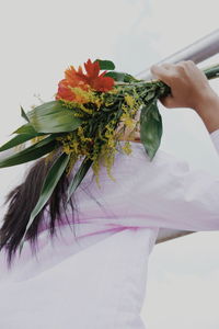 Low angle view of woman holding bouquet while standing by railing against sky