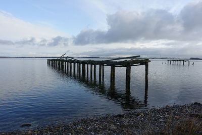 Ruined pier on sea against sky