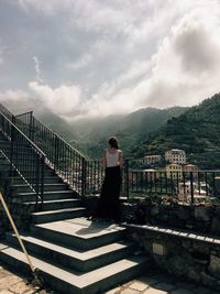 Rear view of woman standing on railing against sky