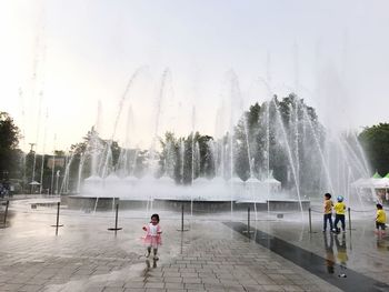 Rear view of people walking on fountain in city against clear sky