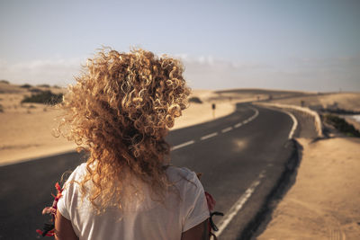 Rear view of woman with curly hair standing on road against sky