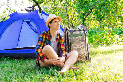 Young woman sitting near camping tent outdoors surrounded by beautiful nature. freelance, sabbatical