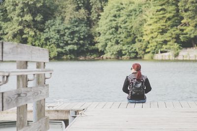 Woman sitting by lake against trees