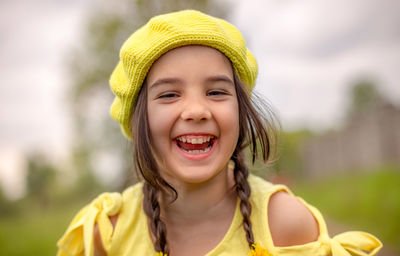 Outdoor shot portrait of a little adorable happy girl in a yellow knitted beret