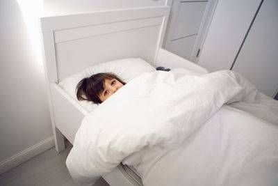 Child boy lies in a white children's bed with a blanket in a room with toy rabbit