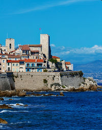 Buildings by sea against blue sky