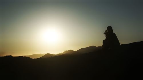 Silhouette woman sitting on mountain against sky during sunset