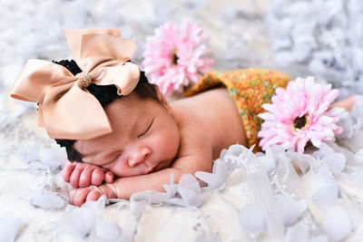 Close-up of cute baby girl with flowers sleeping on bed