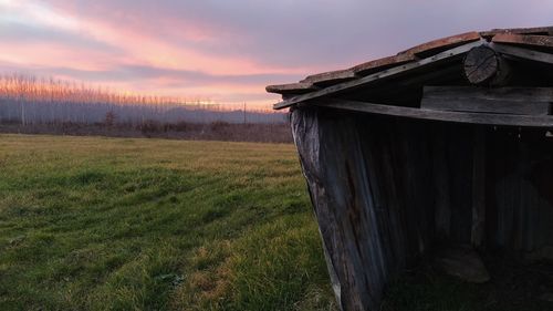 Abandoned built structure on field against sky at sunset